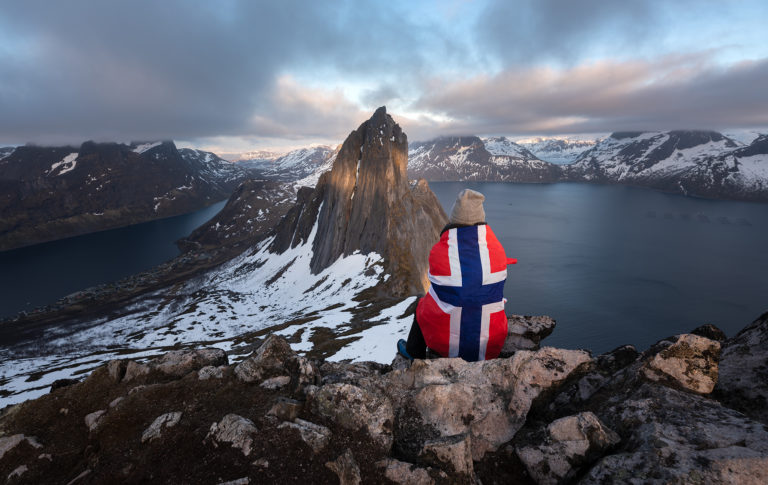 Senja, Norwegia. Dziewczyna owinięta we flagę siedzi z widokiem na Segle. Szczyt Hesten